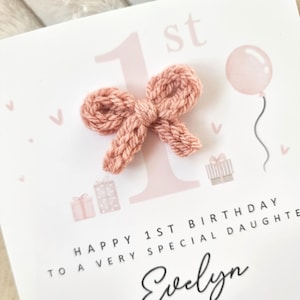 Może przedstawiać: R&oacute;żowa i biała kartka urodzinowa z dzianą kokardką, r&oacute;żowym balonem i tekstem "Happy 1st Birthday to a very special daughter Evelyn".