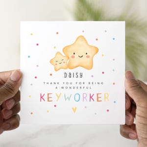 May include: A white card held by hands, with two smiling yellow stars. The card reads "Daisy, Thank you for being a wonderful Keyworker" in colourful text, with scattered dots in various colours.