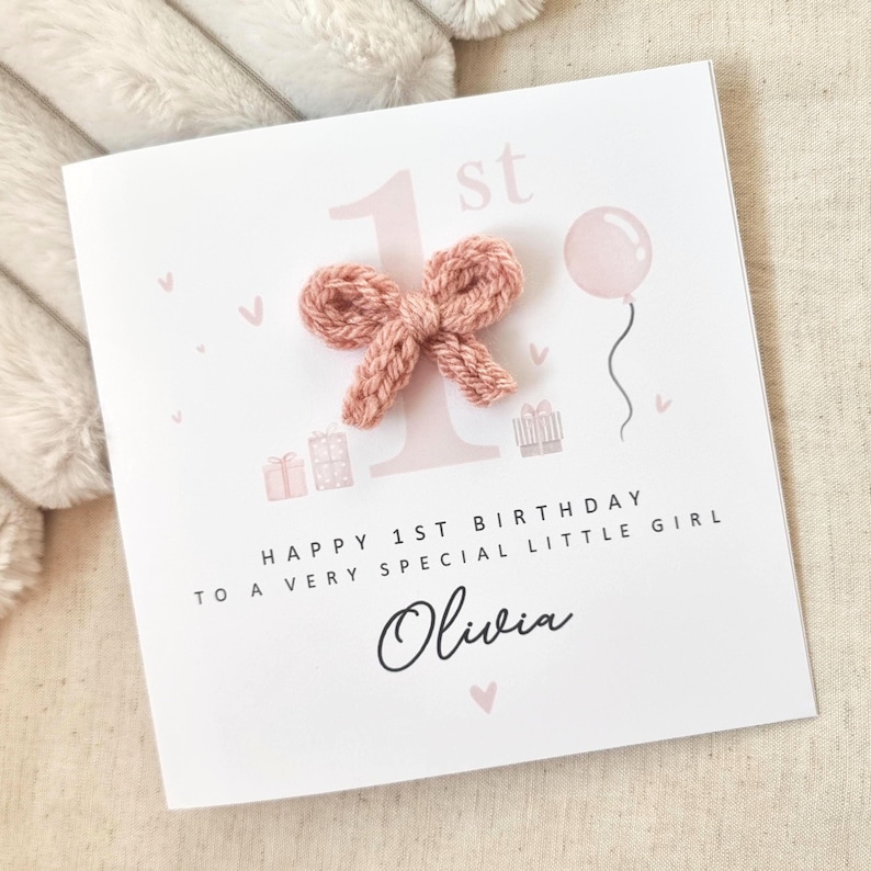 Może przedstawiać: R&oacute;żowa i biała kartka urodzinowa z dzianą kokardką, r&oacute;żowym balonem i tekstem "Happy 1st Birthday to a very special little girl Olivia".