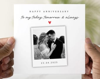 May include: A white anniversary card with the text "HAPPY ANNIVERSARY" and "to my today, tomorrow & always" in black script. A small red heart is above a black and white photo of a couple. The date "23.04.2025" is printed below the photo.