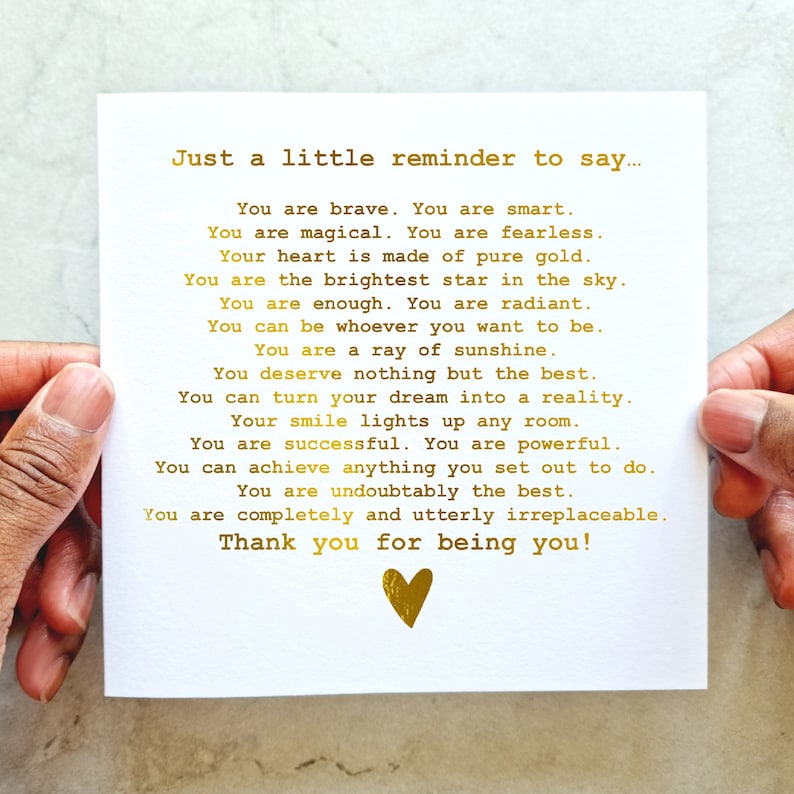 May include: A white card with gold lettering that reads "Just a little reminder to say... You are brave. You are smart. You are magical. You are fearless. Your heart is made of pure gold. You are the brightest star in the sky. You are enough. You are radiant. You can be whoever you want to be. You are a ray of sunshine. You deserve nothing but the best. You can turn your dream into a reality. Your smile lights up any room. You are successful. You are powerful. You can achieve anything you set out to do. You are undoubtedly the best. You are completely and utterly irreplaceable. Thank you for being you!" A gold heart is at the bottom of the card.