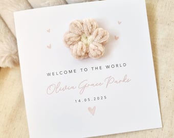 May include: A white card with pink hearts and a pink flower embellishment. The card reads "Welcome to the world Olivia Grace Parks 14.05.2025".