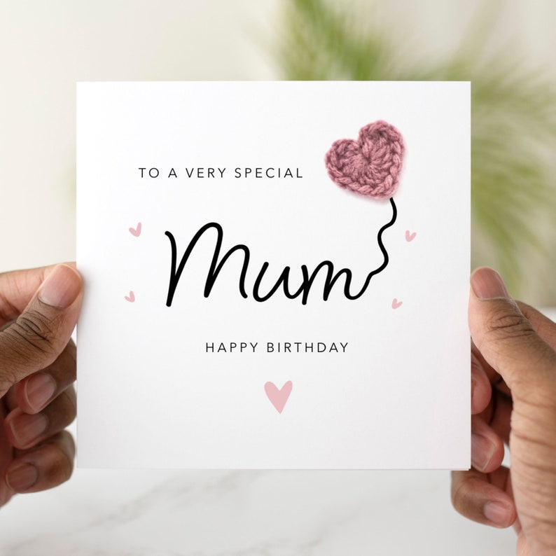 May include: A white card with the words "To a very special Mum Happy Birthday" and a pink crocheted heart with a string attached to it.