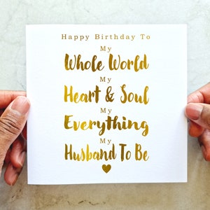 May include: A white card with gold foil lettering that reads "Happy Birthday To My Whole World My Heart & Soul My Everything My Husband To Be".