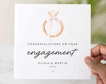 May include: White engagement card featuring a watercolor illustration of a diamond ring with a pink bow. The card reads "Congratulations on your engagement" with the names Olivia & Martin and the year 2025.