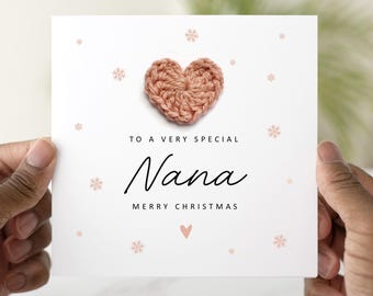 May include: A white greeting card with a crocheted heart and the words "To a very special Nana Merry Christmas". The card has small pink snowflakes and a heart design.