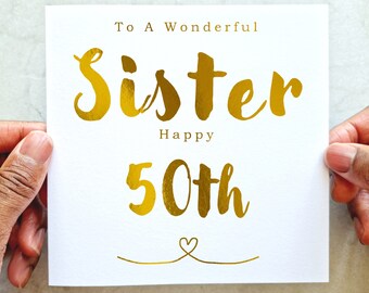 May include: A white card with gold foil lettering that reads "To A Wonderful Sister Happy 50th" with a small heart at the bottom.