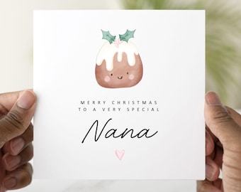May include: A white Christmas card with a watercolor illustration of a smiling Christmas pudding topped with holly. The card reads "Merry Christmas to a very special Nana" with a pink heart.