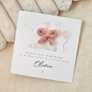 Może przedstawiać: R&oacute;żowa i biała kartka urodzinowa z r&oacute;żową dzianą kokardką, r&oacute;żowym balonem i tekstem "Happy 1st Birthday to a very special little girl Olivia".