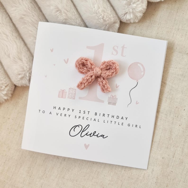 Może przedstawiać: R&oacute;żowa i biała kartka urodzinowa z r&oacute;żową dzianą kokardką, r&oacute;żowym balonem i tekstem "Happy 1st Birthday to a very special little girl Olivia".