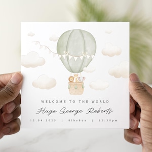 Op de afbeelding: Een groene en witte luchtballon met dierlijke passagiers, omringd door wolken. De tekst luidt "Welkom op de wereld Hugo George Roberts 12.04.2025 | 8lbs 8oz | 12:30pm"