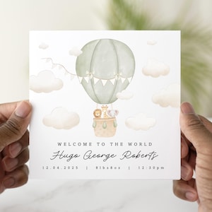 Op de afbeelding: Een groene en witte luchtballon met een giraffe, een leeuw en een olifant erin. De ballon zweeft in de lucht met witte wolken. De tekst "WELCOME TO THE WORLD Hugo George Roberts 12.04.2025 | 8lbs 8oz | 12:30pm" staat onder de ballon.