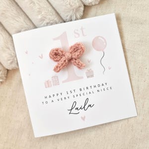 Może przedstawiać: R&oacute;żowa i biała kartka urodzinowa z r&oacute;żową dzianą kokardką, r&oacute;żowym balonem i tekstem "Happy 1st Birthday to a very special niece Laila".