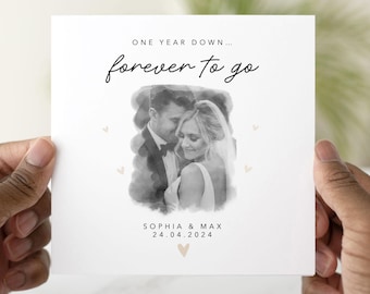 May include: A square, white card with a black and white photo of a couple. The text "ONE YEAR DOWN... forever to go" is written in black script. The names "SOPHIA & MAX" and the date "24.04.2024" are also included.