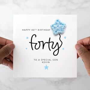 Peut inclure: Une carte blanche avec le texte "Happy 40th Birthday forty" et "To a special son Kevin" avec une étoile bleue en crochet sur le dessus.