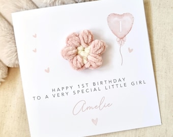 May include: A pink and white flower with a pink heart balloon with the number 1 on it. The card reads "Happy 1st Birthday to a very special little girl Amelie".