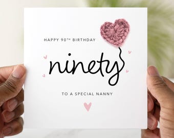 May include: A white card with pink hearts and the text "Happy 90th Birthday ninety to a special nanny". A pink crocheted heart is attached to the top of the card.