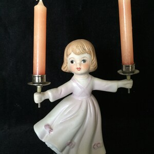 May include: A porcelain figurine of a girl in a pink dress holding two candlesticks with pink candles.