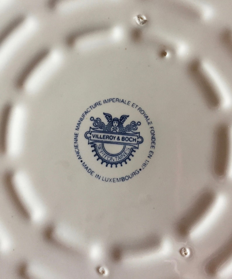 May include: A white ceramic plate with a blue and white logo that reads "ANCIENNE MANUFACTURE IMPERIALE ET ROYALE FONDEE EN 1767 VILLEROY & BOCH SEPTEONTAINES MADE IN LUXEMBOURG. 19", indicating the origin and maker of the plate.