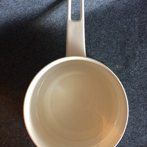 May include: White ceramic saucepan with a single handle. The handle has a small opening in the middle.