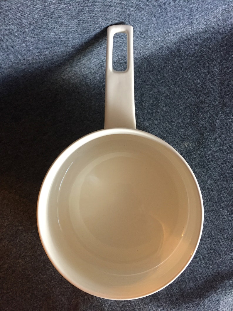 May include: White ceramic saucepan with a single handle. The handle has a small opening in the middle.