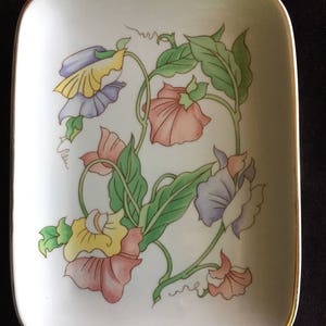 May include: A rectangular, off-white ceramic dish with a floral design. The design features colorful sweet pea flowers in shades of pink, yellow, and purple, with green leaves and gold trim. The dish has rounded corners.