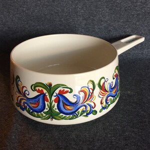 May include: White ceramic pot with a blue, red, yellow, and green floral design featuring stylized birds. The pot has a white plastic handle.