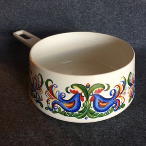 May include: White ceramic saucepan with a blue handle and a colorful folk art design featuring birds and floral motifs.