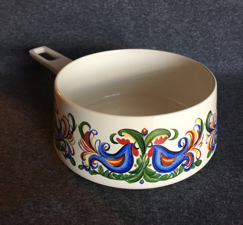 May include: White ceramic saucepan with a blue handle and a colorful folk art design featuring birds and floral motifs.