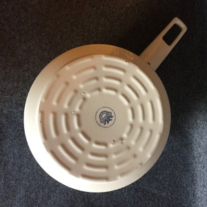 May include: White enameled cast iron skillet with a black and blue logo on the bottom. The logo reads "Made in Germany,  Original Staub,  Since 1974".