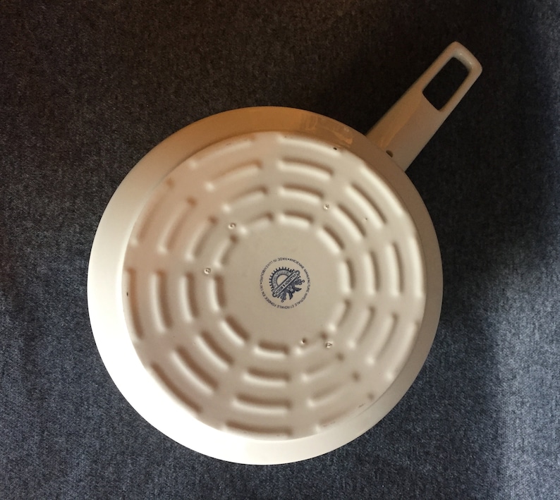 May include: White enameled cast iron skillet with a black and blue logo on the bottom. The logo reads "Made in Germany,  Original Staub,  Since 1974".