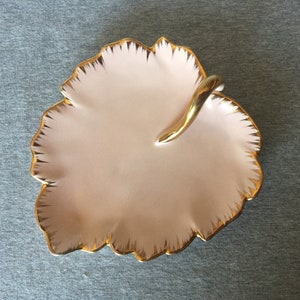 May include: A pink ceramic dish with a gold rim and a gold handle. The dish is shaped like a leaf and has a scalloped edge.