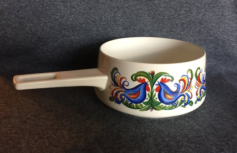 May include: White ceramic saucepan with a white handle and a blue, red, green, and yellow rooster design around the rim.