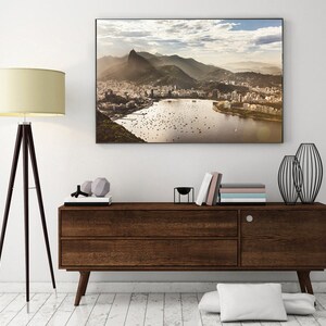 May include: A framed photograph of a city skyline with a mountain in the background. The city is on a peninsula with a body of water in front of it. The photo is hanging on a white wall above a dark brown wooden dresser.