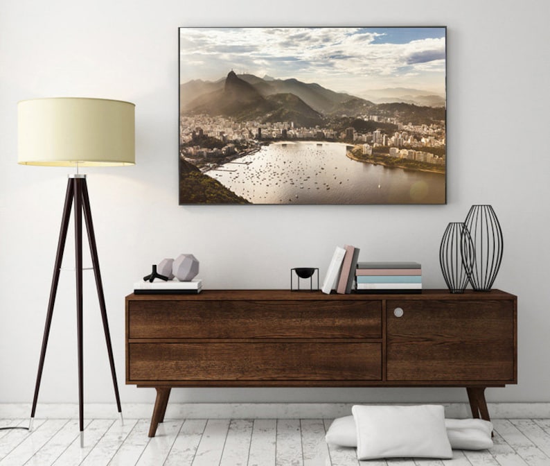 May include: A framed photograph of a city skyline with a mountain in the background. The city is on a peninsula with a body of water in front of it. The photo is hanging on a white wall above a dark brown wooden dresser.