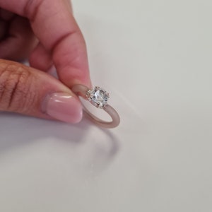 K&ouml;nnte beinhalten: Ein silberner Ring mit einem gro&szlig;en, klaren, runden Edelstein. Das Ringband hat eine helle, ged&auml;mpfte rosa Farbe. Der Edelstein wird von einer silbernen Fassung gehalten.