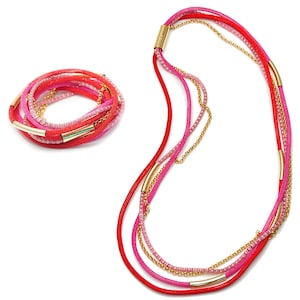 May include: A multi-strand necklace and bracelet set featuring pink, red, and gold. The necklace has a long, layered design with a gold chain and multiple strands of pink and red cord. The bracelet is a similar design, but shorter and with a single gold bar.