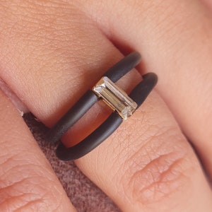 Puede incluir: Un anillo de silicona negro con una piedra rectangular transparente engastada en oro.