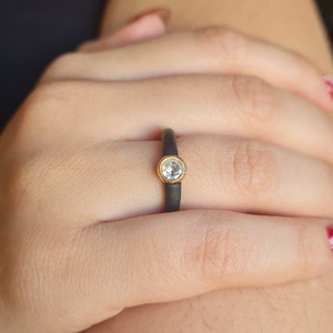 May include: A black ceramic ring with a gold band and a clear round gemstone.