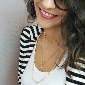 May include: A woman wearing a black and white striped blazer with a gold necklace featuring a small crystal pendant and star charms.