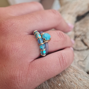 Op de afbeelding: Twee ringen met blauwe en gouden accenten. De bovenste ring heeft een grote blauwe edelsteen met een gouden zetting. De onderste ring is een band van blauwe edelstenen met gouden accenten.