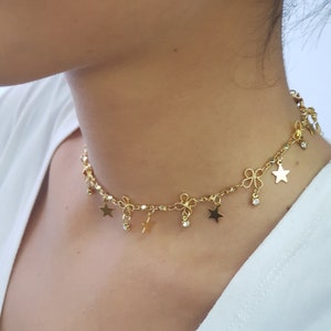 May include: A gold chain choker necklace with star and bow charms. The necklace has a delicate chain and features small, dangling stars and bows.