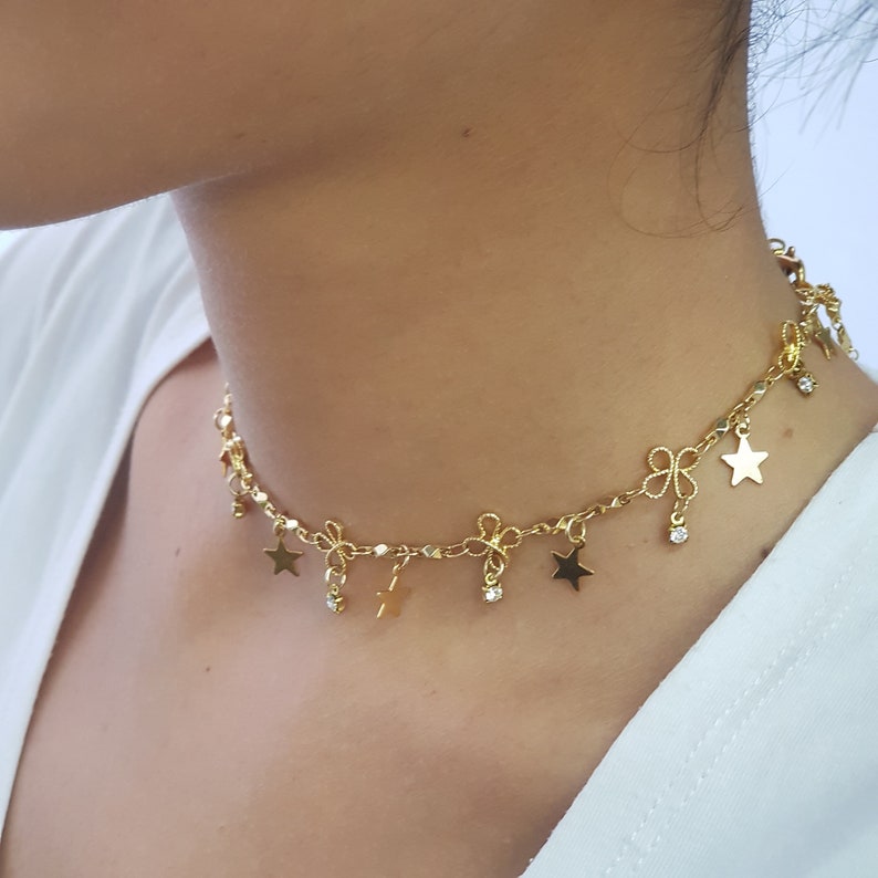 May include: A gold chain choker necklace with star and bow charms. The necklace has a delicate chain and features small, dangling stars and bows.