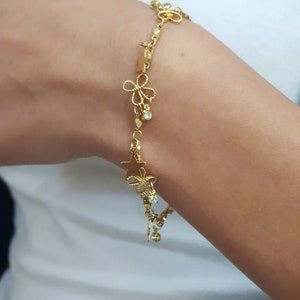 May include: A gold chain bracelet with star and flower charms and clear crystal accents.