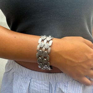 Pode incluir: Um bracelete de prata com um design de corrente de elos, apresentando múltiplas filas de elos metálicos redondos e texturizados.