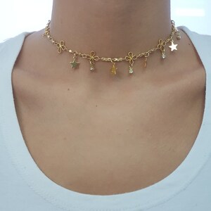 May include: A gold choker necklace with a delicate chain and star-shaped charms. The necklace has small, clear rhinestones between the charms.