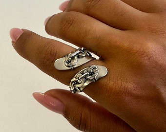 May include: A silver ring with a chain design. The ring is made of two pieces that wrap around the finger.