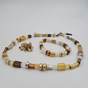 May include: A set of two necklaces made with white, gold, silver, and brown beads. The necklace is made with square and round beads. The smaller necklace is a bracelet.