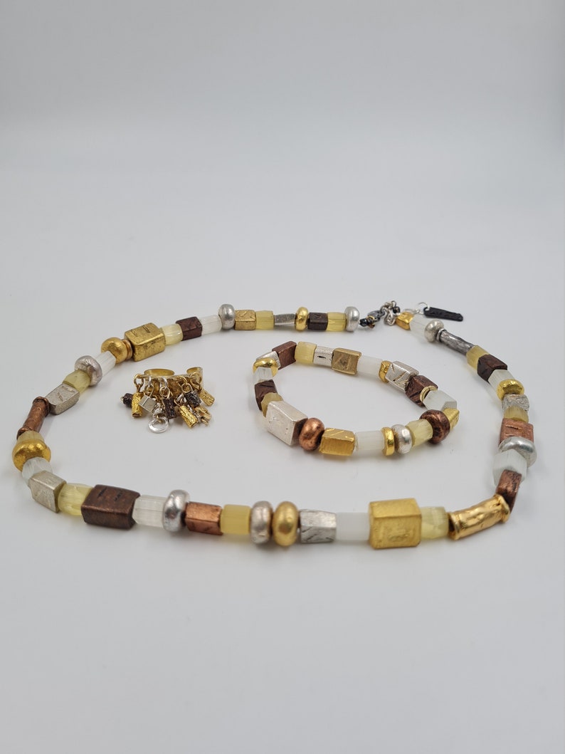 May include: A set of two necklaces made with white, gold, silver, and brown beads. The necklace is made with square and round beads. The smaller necklace is a bracelet.