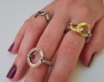 Pode incluir: Três anéis de prata com um design de elo de corrente. O anel do dedo do meio tem dois círculos ligados com um acabamento de esmalte verde e dourado.